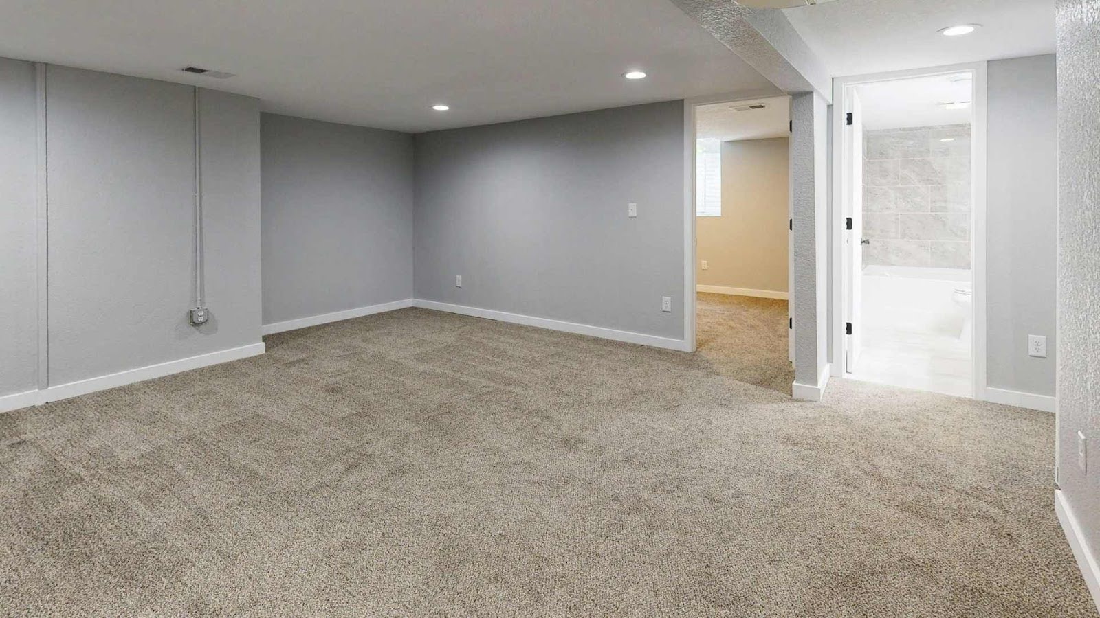 Finished basement with grey walls, recessed lights, carpet flooring, and bathroom doorway.