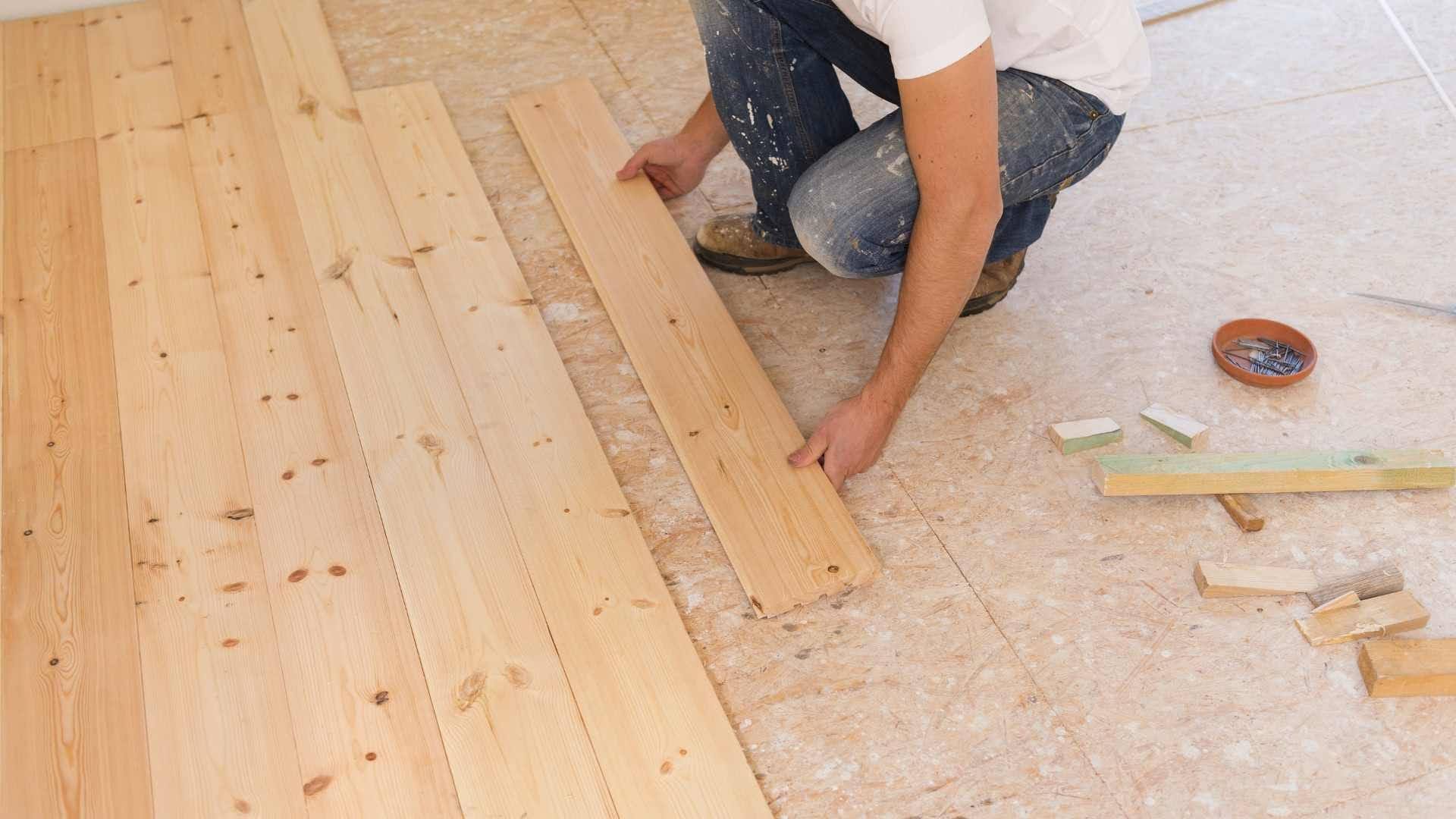 Worker positioning a pine floorboard next to newly laid subfloor planks