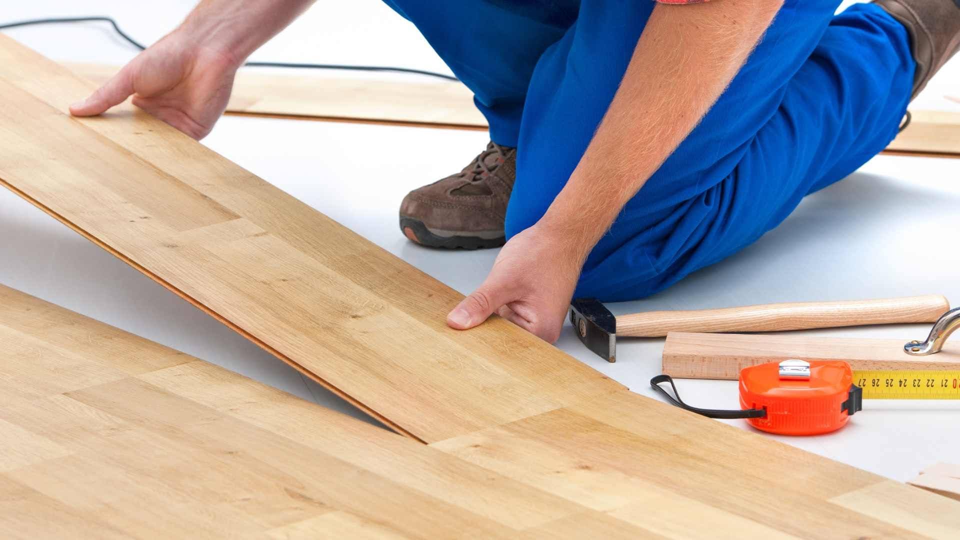 Worker fitting a wood plank while installing hardwood flooring