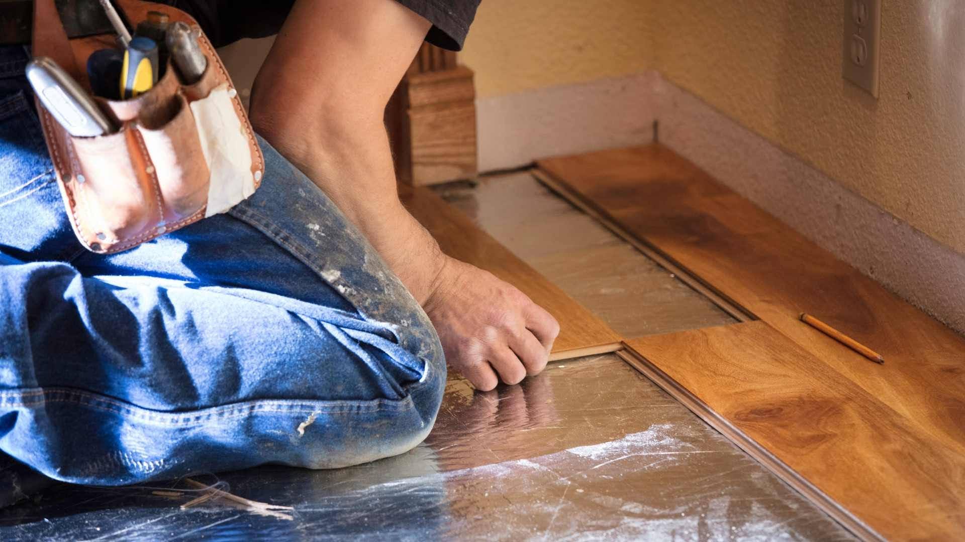 Installer pressing a wood floor board into place near a wall outlet