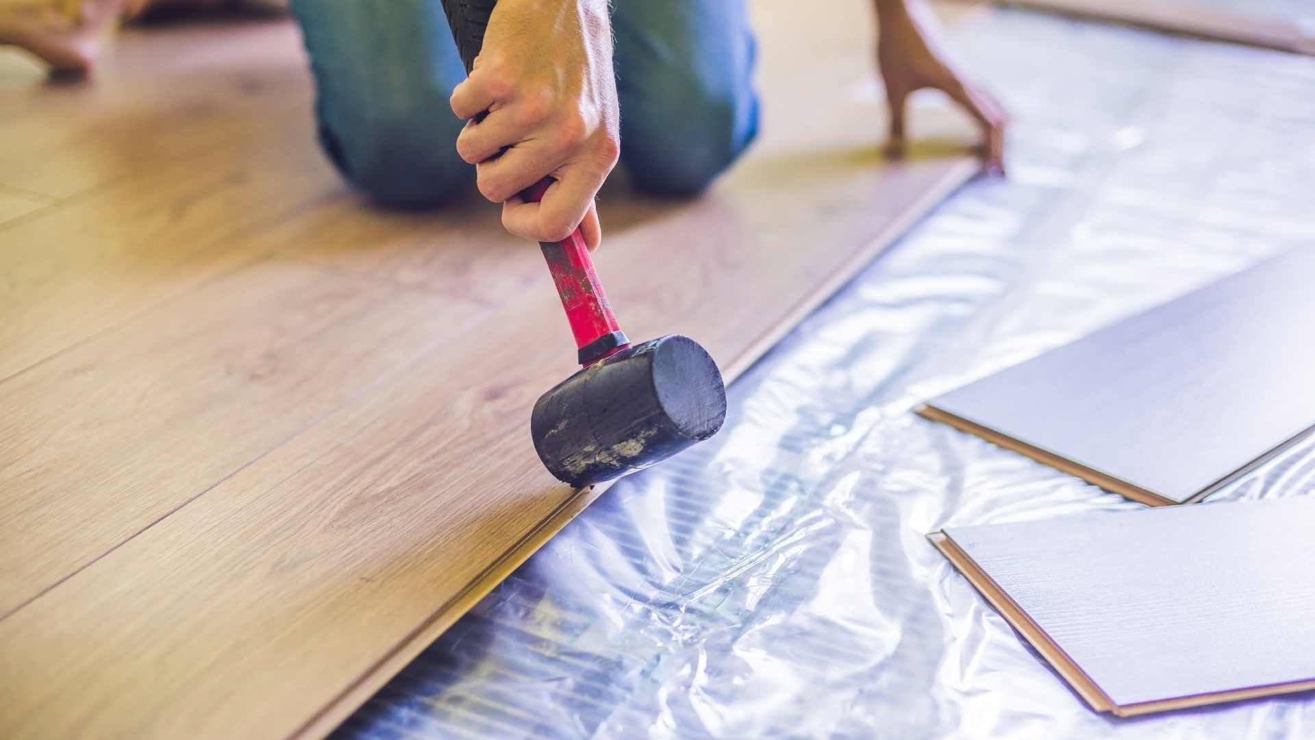 Rubber mallet tapping a laminate floor plank into place over underlayment