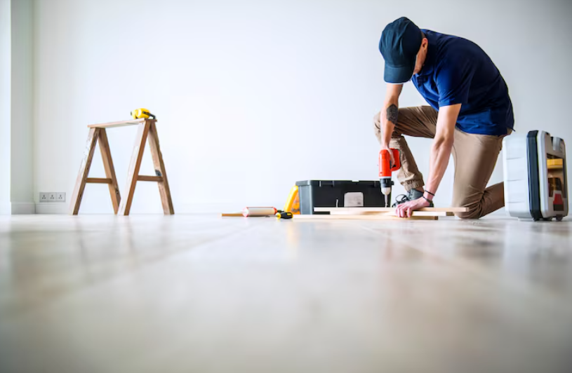 Floor installer using a power drill to install hardwood flooring.